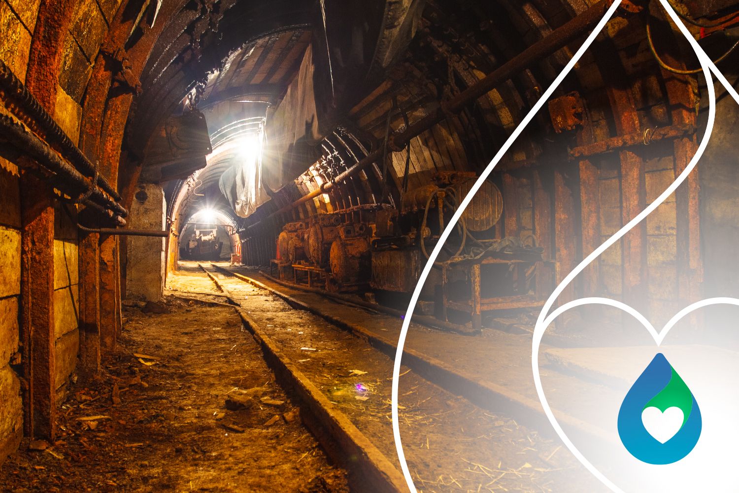 Galería interior de una mina con rieles, tuberías y maquinaria a los costados, iluminada por focos al fondo del túnel