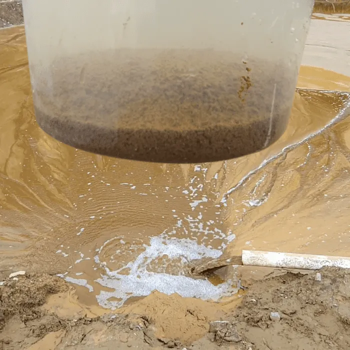 Balde vertiendo agua clarificada sobre una superficie de relave en una operación minera